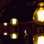 A bride poses elegantly in dramatic lighting surrounded by glowing bulbs, creating a unique wedding portrait.