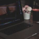 A cozy workspace featuring a laptop, coffee cup, and artificial flowers, ideal for remote work.