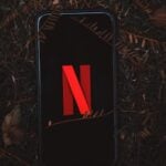 Close-up of a smartphone displaying Netflix on a leafy outdoor ground.