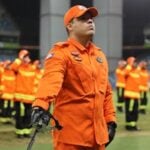 Group of firefighters in orange uniforms during a formal ceremony at night.
