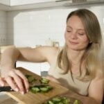 Smiling woman cutting cucumbers in a bright kitchen, a modern take on healthy lifestyle.